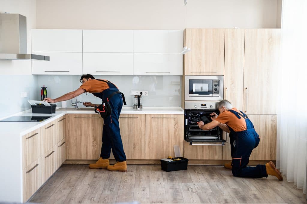 Repair. Two handymen, workers in uniform fixing, installing furniture and equipment in the kitchen, using screwdriver indoors. Furniture repair and assembly concept